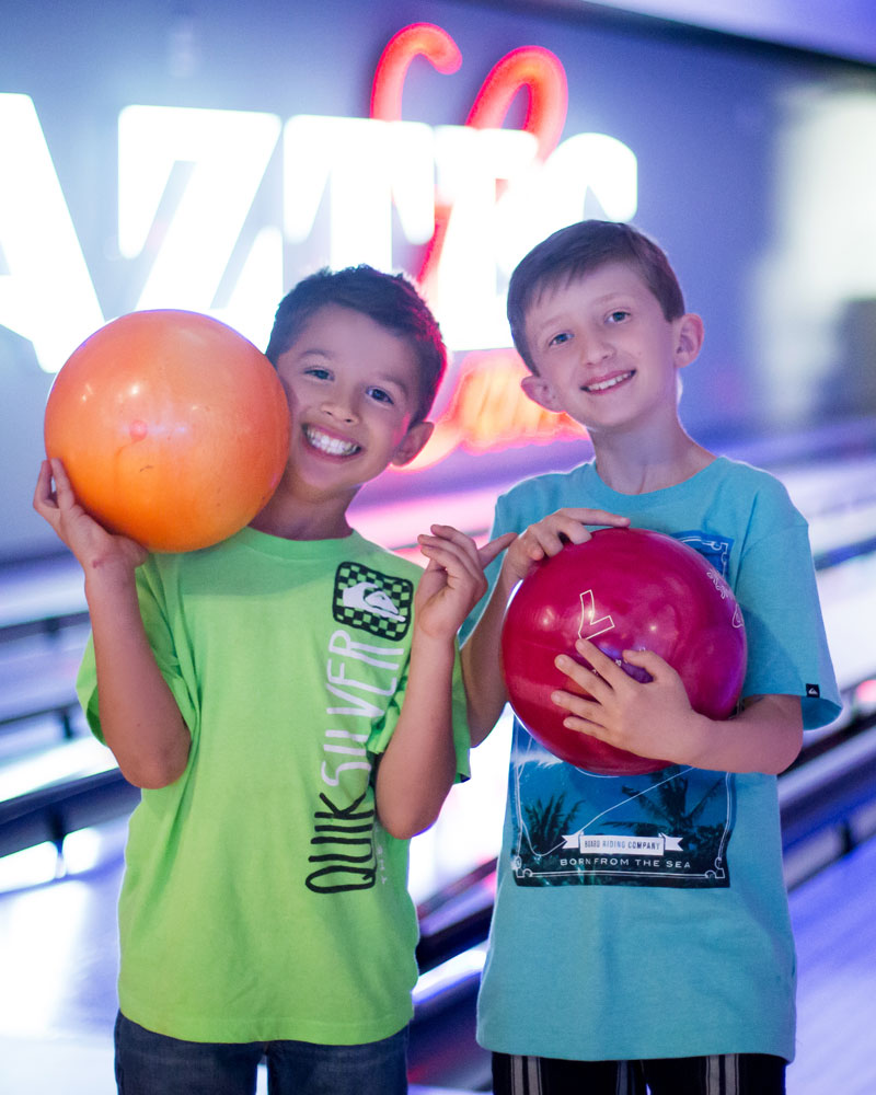 Two smiling boys holding bowling balls at Aztec Lanes